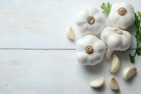 Fresh garlic bulbs and cloves with green parsley on white wooden background for cooking and culinary preparations.