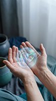 Hands holding transparent soap bubble with rainbow reflections in cozy bedroom setting with morning light and soft blue textiles.
