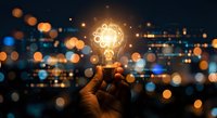 Hand holding glowing lightbulb with gear mechanism against bokeh city lights background representing innovation and creative business solutions.
