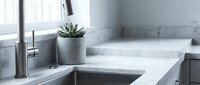Modern kitchen sink with white marble countertop, stainless steel faucet, and potted succulent plant for home interior design and renovation projects.