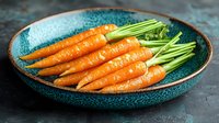 Fresh organic carrots with green tops arranged on turquoise ceramic plate against dark background, raw vegetables for healthy eating and cooking.