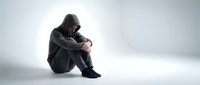 Young man in hoodie sitting alone in contemplative pose against white background expressing sadness, depression, mental health struggles and emotional isolation.