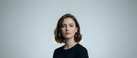 Professional young Caucasian businesswoman with short brown hair wearing black top against neutral background for corporate branding and marketing materials.