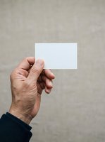 Male hand holding blank white card against neutral gray background, suitable for business card mockups and branding presentations.