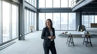 Confident businesswoman in dark blazer standing in modern empty office space with floor-to-ceiling windows overlooking city skyline, professional workspace design.