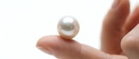 A woman's hand holding a lustrous white pearl against a clean white background, showcasing luxury jewelry and gemstone elegance for design and commercial use.