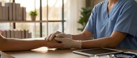 Healthcare professional in blue scrubs providing compassionate patient care and consultation in modern medical office setting with natural lighting.