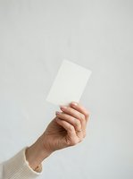 Hand holding blank white card against neutral background, suitable for business branding, marketing mockups, and promotional material design.