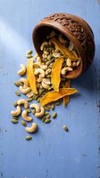 Ornate wooden bowl spilling mixed nuts and dried mango slices on rustic blue surface for healthy snacking and cooking ingredients.