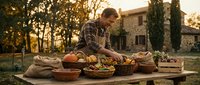 Smiling middle-aged Caucasian male farmer arranging fresh harvested vegetables on rustic wooden table outdoors at golden hour farm setting.