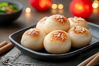 Fresh homemade Asian buns with sesame seeds served on black plate with chopsticks. Soft steamed dough with golden crust in moody lighting with bokeh.