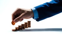 Businessman in blue suit placing coin on stacked coins, representing financial growth, investment, savings, and wealth accumulation for business concepts.