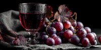 Glass of red wine with fresh purple grapes on rustic linen fabric against dark background for winery marketing and culinary photography projects.