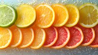 Fresh citrus fruit slices arranged in rainbow gradient from lime, lemon, orange to grapefruit with water drops on dark background, macro food photography.