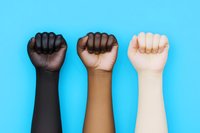 Raised fists of different skin tones showing unity, solidarity and racial equality against bright blue background, powerful social justice concept.