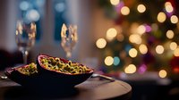 Festive appetizers in black ceramic bowl with champagne flutes against blurred Christmas tree lights creating magical bokeh atmosphere.