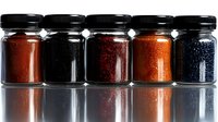 Glass jars filled with colorful caviar varieties arranged in row showing red, black and orange fish roe with reflection on glossy surface. Luxury gourmet seafood concept.