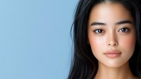 Young Asian woman with natural makeup and flowing dark hair against soft blue background for beauty and skincare campaigns.