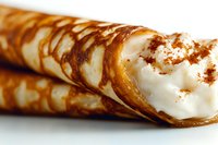 Freshly baked crispy crepe rolls filled with sweet whipped cream and dusted with cinnamon powder on white background, close up view of dessert pastry.