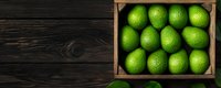 Fresh green limes in rustic wooden box on dark wooden background, top view. Natural citrus fruits for cooking, cocktails and healthy eating.