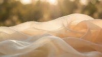 Flowing cream and gold silk fabric waves in soft sunlight with blurred bokeh background, suitable for luxury, fashion, and elegant design projects.