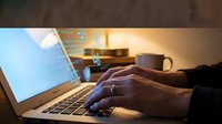Professional businessman typing on laptop computer in modern office workspace with warm lighting and coffee cup creating productive work environment.