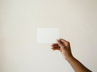Male hand with medium brown skin tone holding blank white card against neutral background for branding, marketing, and promotional mockup purposes.