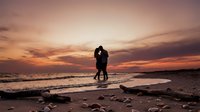 Romantic couple silhouette embracing on beach at sunset with dramatic colorful sky and ocean waves for wedding anniversary valentine love concept.