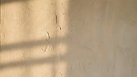 Textured beige wall with natural sunlight casting shadows and creating abstract patterns, suitable for backgrounds and design projects.