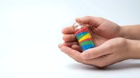 Hands gently holding colorful rainbow striped wooden blocks in protective cupped gesture on white background symbolizing care diversity inclusion support.