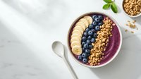 Acai bowl with granola, blueberries and banana slices on marble surface, overhead view for healthy breakfast and smoothie bowl content.