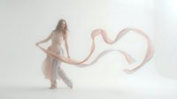 Young woman in flowing dress with pink fabric ribbon dancing gracefully in soft ethereal light creating dreamy romantic atmosphere for fashion concepts.