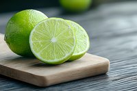 Fresh green limes on wooden cutting board, whole and halved citrus fruits showing juicy pulp texture against dark wooden table background.