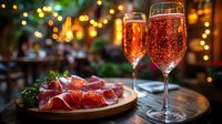 Elegant champagne glasses filled with sparkling wine alongside gourmet charcuterie board with prosciutto and herbs against warm bokeh lights backdrop.