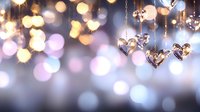 Shiny heart-shaped pendants hanging on chains against blurred bokeh lights background in soft purple and golden tones, creating romantic atmosphere.