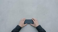 Hands holding black smartphone on concrete surface from above, mobile device technology concept for digital communication and modern lifestyle.