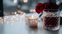 Romantic evening setting with crystal glass of red wine, glowing candle holder, and red rose against soft bokeh lights background. Cozy Valentine's Day atmosphere.
