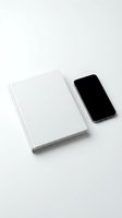 White hardcover notebook and smartphone with blank screen on white background, minimalist mockup for branding and design projects.