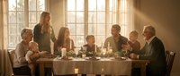 Multi-generational family gathering around dining table for holiday meal with warm sunlight streaming through windows creating cozy atmosphere.