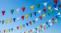 Colorful triangular bunting flags in red, yellow, green, blue and white hanging against clear blue sky for festive celebrations and outdoor events.