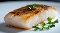 Seared white fish fillet with caramelized crust and fresh parsley garnish on white plate, close-up view showing moist, flaky texture in natural lighting.