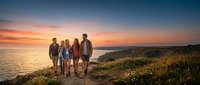 Group of four people standing on coastal cliff at sunset, enjoying scenic ocean view and golden hour landscape during outdoor adventure.