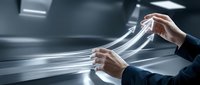 Businessman hands pulling transparent plastic wrap or film material in modern industrial setting for packaging and protection applications.