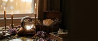 Mystical witch altar with crystal ball, candles, herbs and magical tools in warm golden sunlight for spiritual practices and divination rituals.
