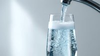 Fresh clean water pouring from modern faucet into transparent glass with bubbles and splash, healthy hydration and drinking water concept.