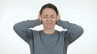 Young Caucasian woman covering ears with hands showing stressed expression wearing gray sweater on white background for mental health concepts.