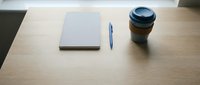 Minimalist workspace setup with closed notebook, pen, and coffee cup on wooden desk for business and productivity concepts.