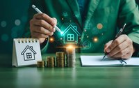 Professional businessman calculating mortgage payments with digital house hologram, coins and documents on desk for real estate investment planning.