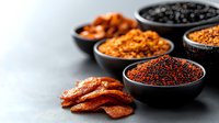 Assorted spices and seasonings in black ceramic bowls on dark concrete background, red chili flakes and dried peppers for cooking and food preparation.