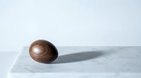 Smooth wooden egg-shaped object casting shadow on white marble surface, minimalist composition for modern interior design and zen meditation concepts.